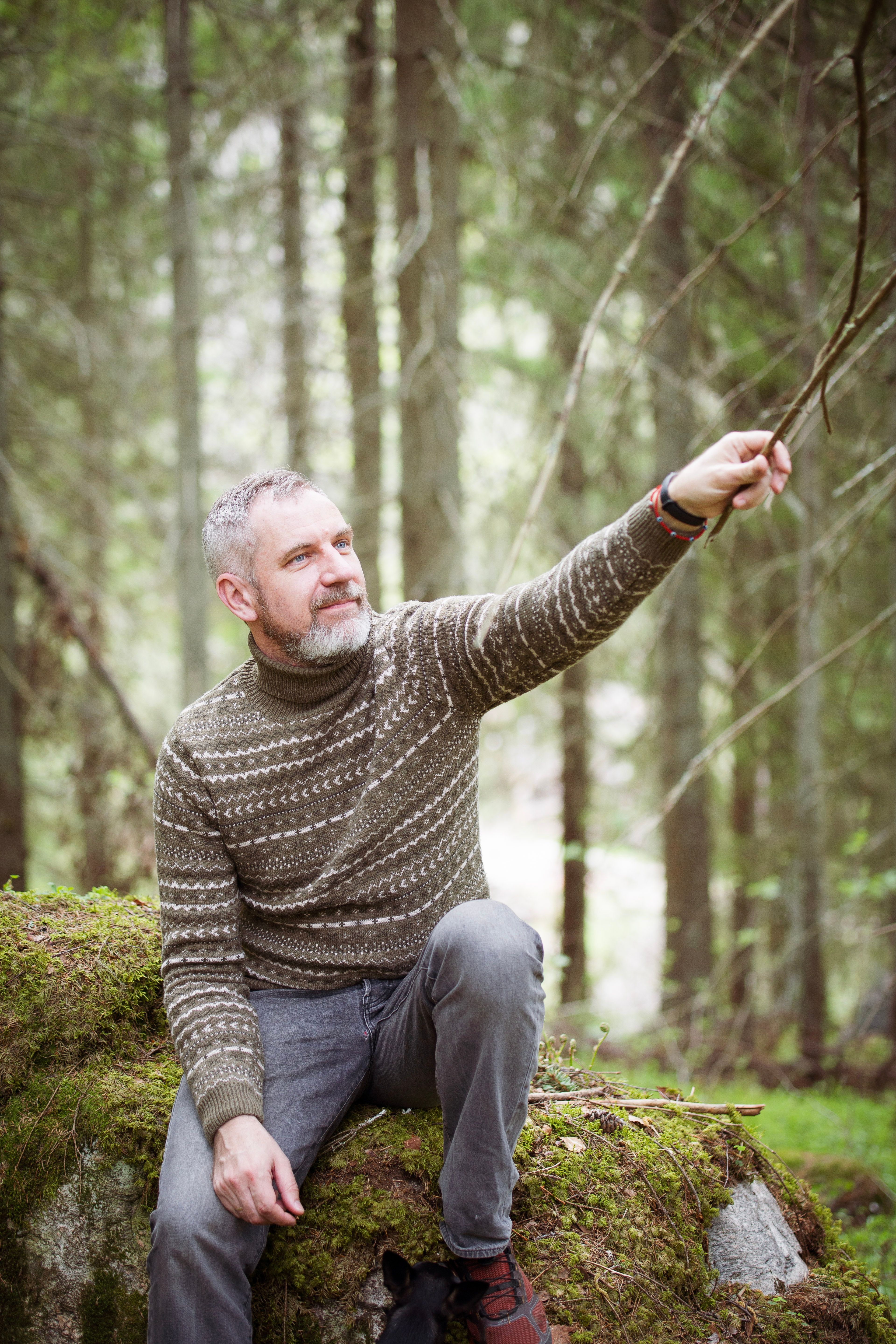 Man with gray hair relaxing on moss-covered rock in a forest setting, enjoying nature.