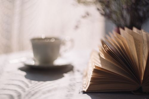 Free An open book on a sunlit table with a blurred coffee cup in the background creates a cozy, reflective atmosphere. Stock Photo