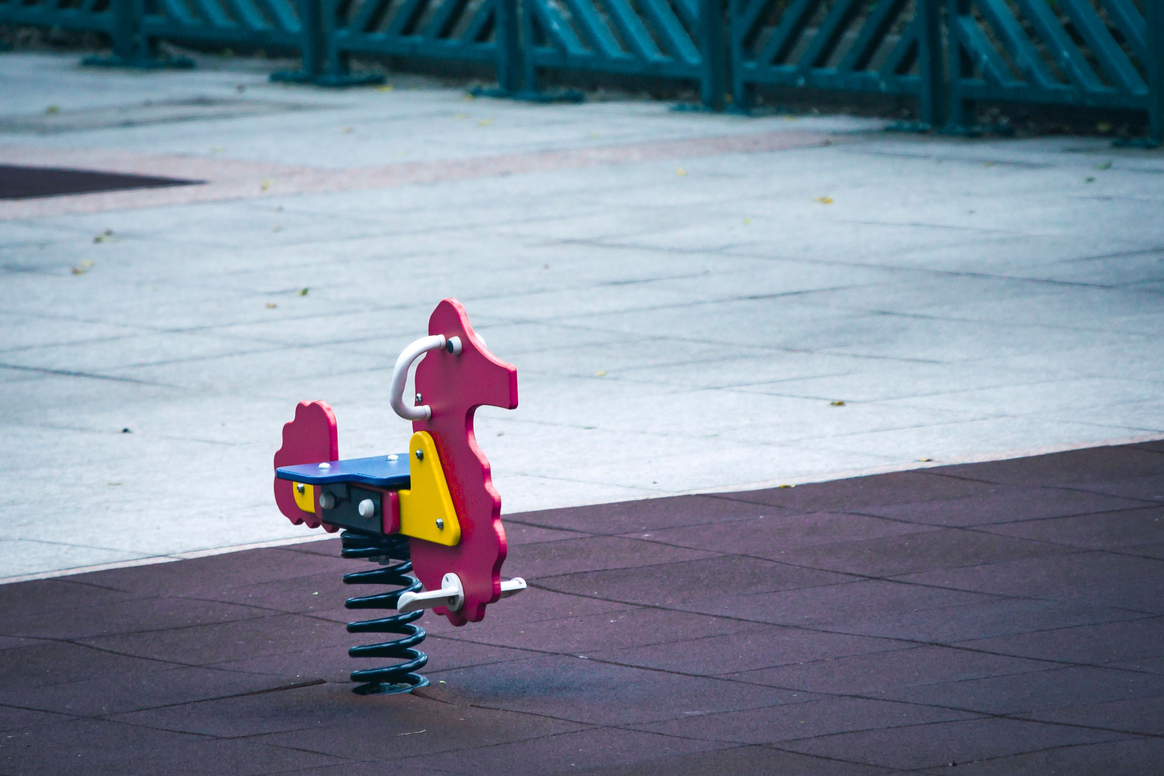 A vibrant, spring-mounted playground horse toy on an empty rubber matting surface in a park.
