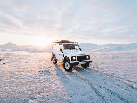 White 4x4 vehicle driving through snow-covered landscape in Iceland at sunset.