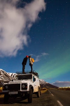 Couple kissing under the northern lights on a Land Rover in Iceland's winter landscape.