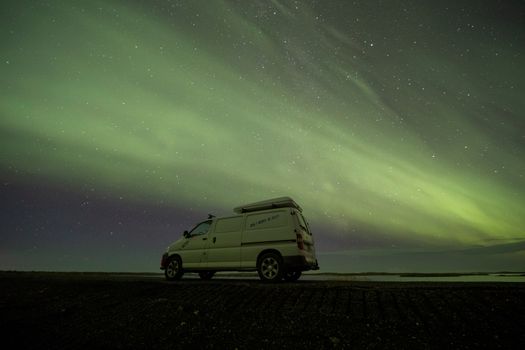 A camper van under the stunning aurora borealis at night in Iceland's wilderness.