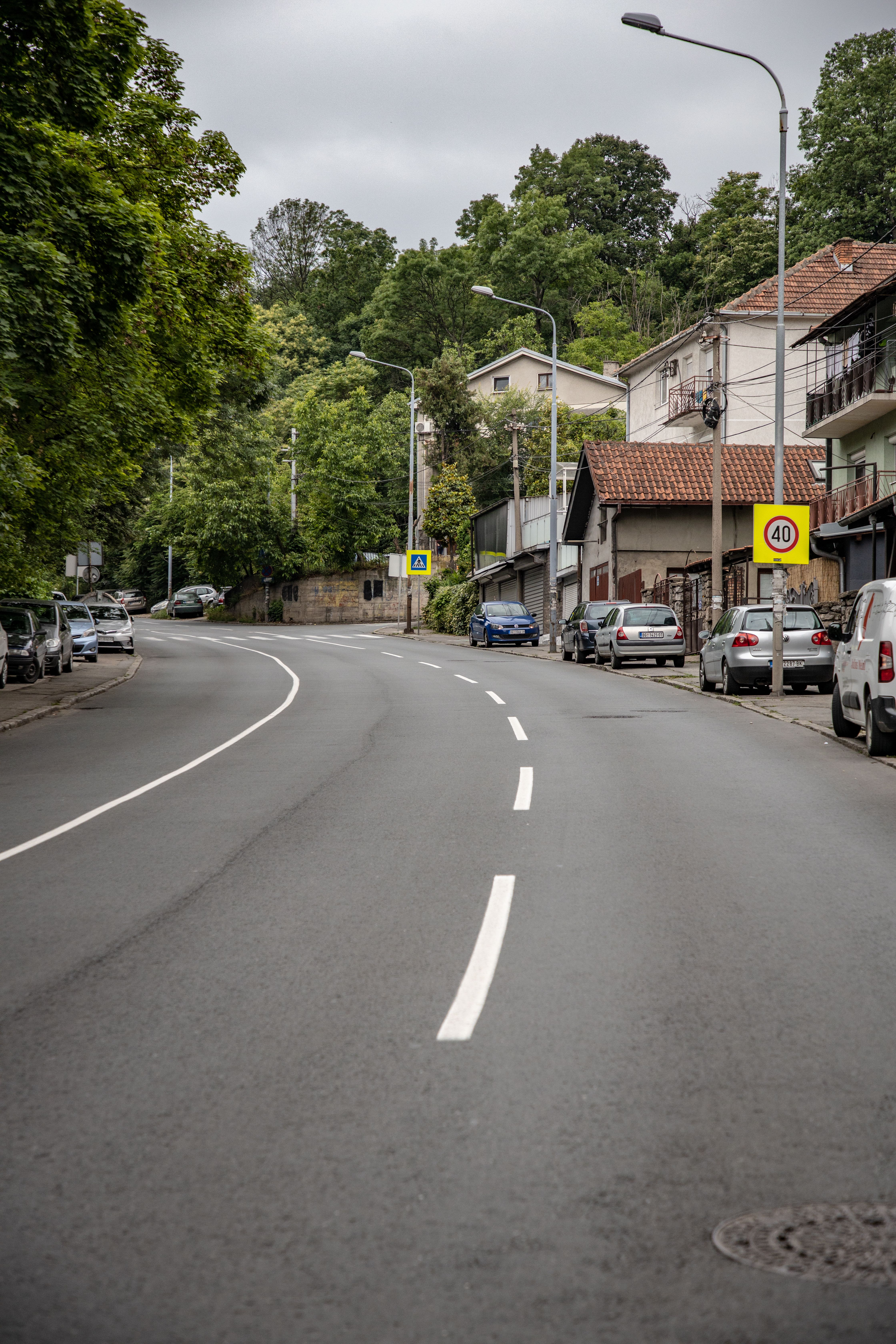 A suburban street with road signs and parked cars, surrounded by greenery.