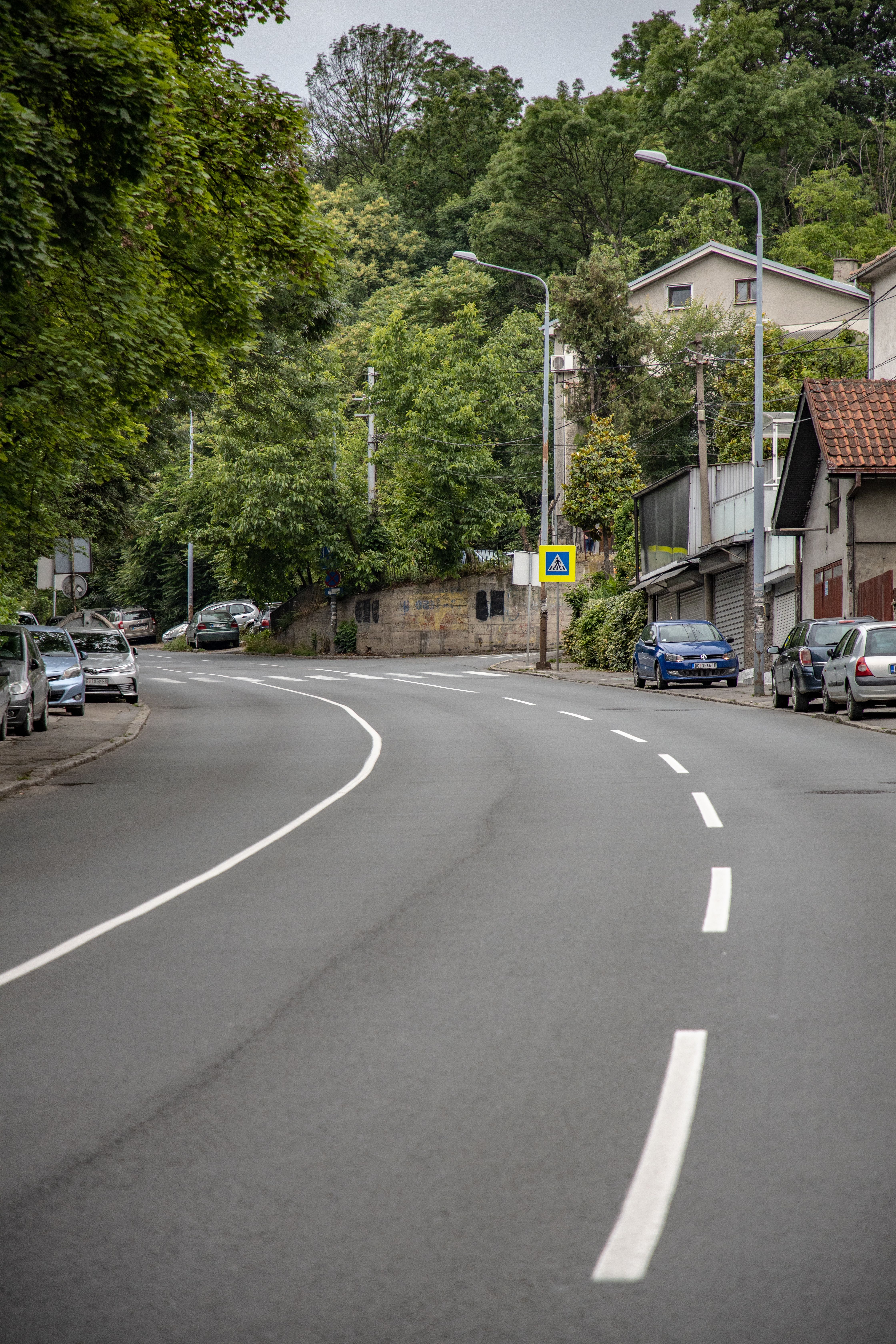Curved urban street with parked cars and abundant greenery lining the road.
