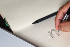 A person writing in a notebook, focusing on pencil sketching and typography design.