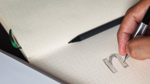 A person writing in a notebook, focusing on pencil sketching and typography design.