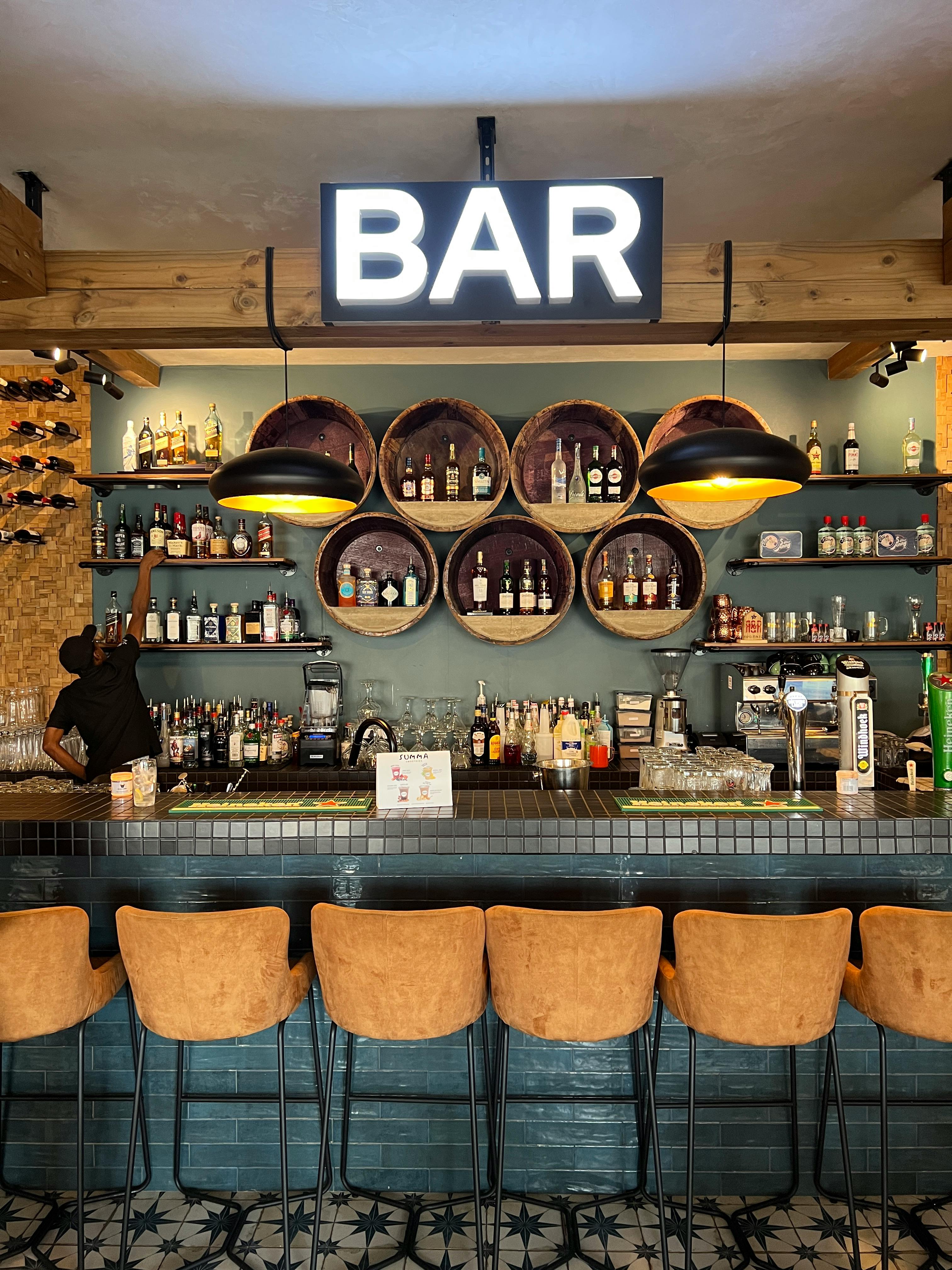 Warm inviting bar scene with bottles, chairs, and a bright sign.
