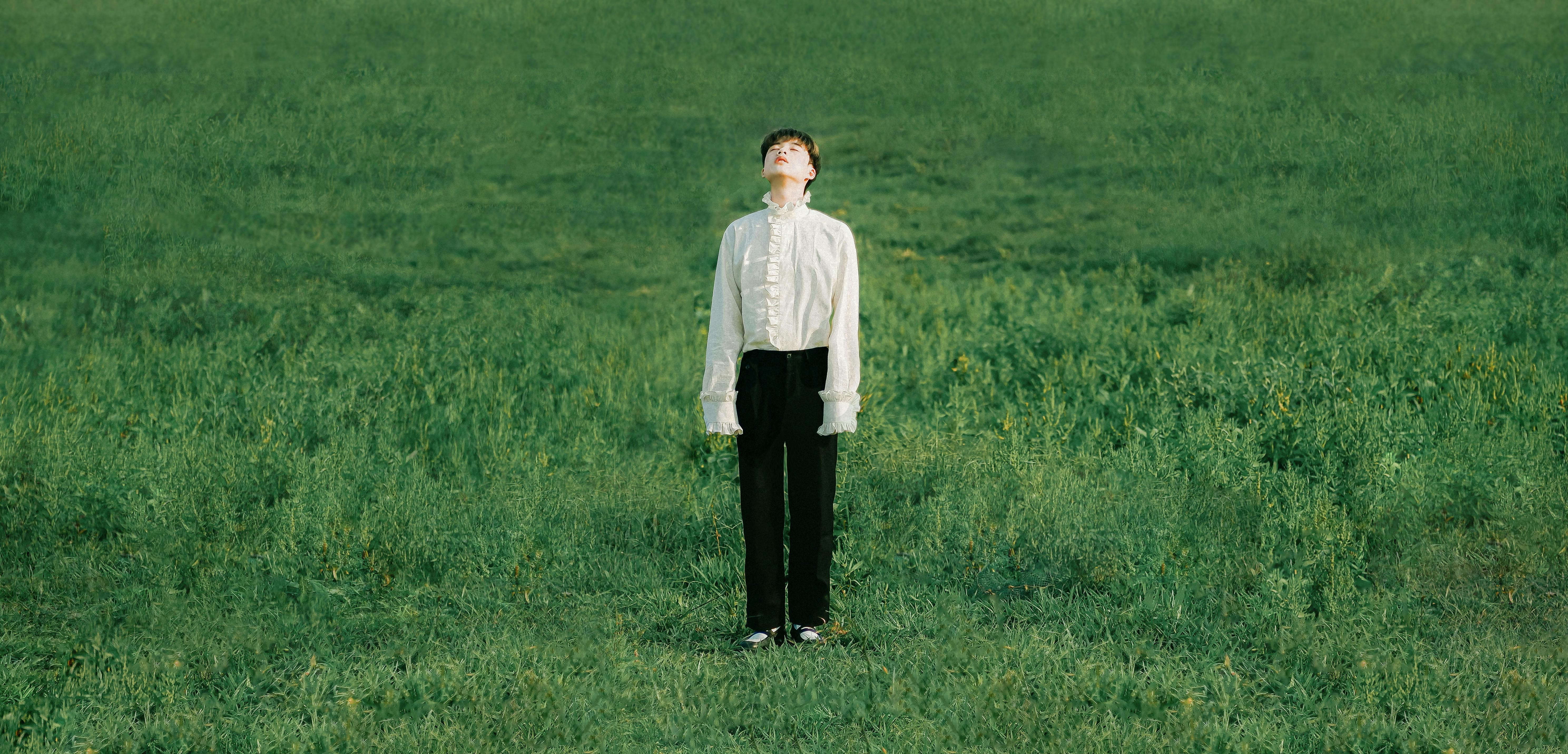 Man in a white shirt stands in a green grass field, posing creatively.
