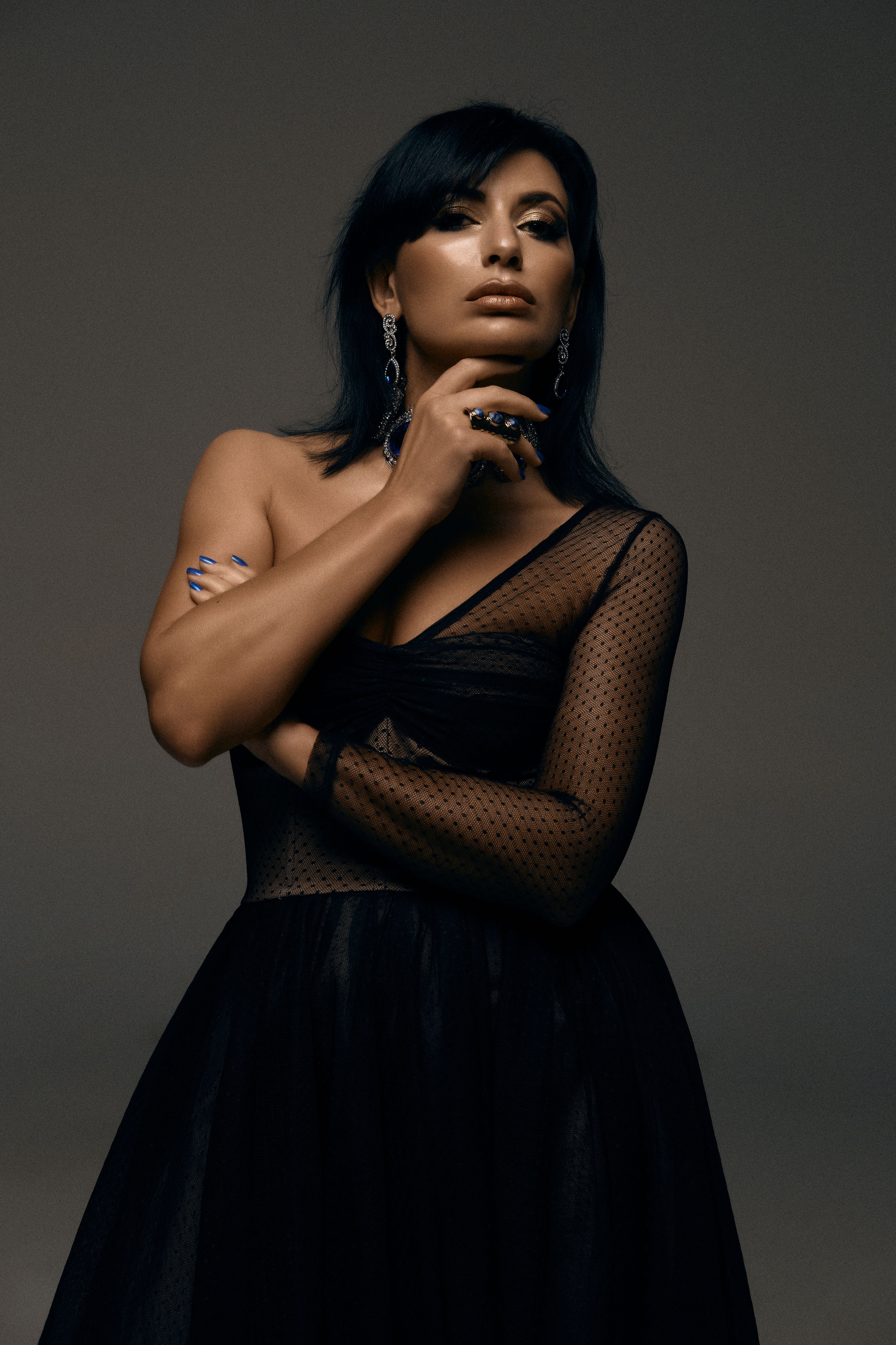 Stylish woman posing in a black dress against a gray background.