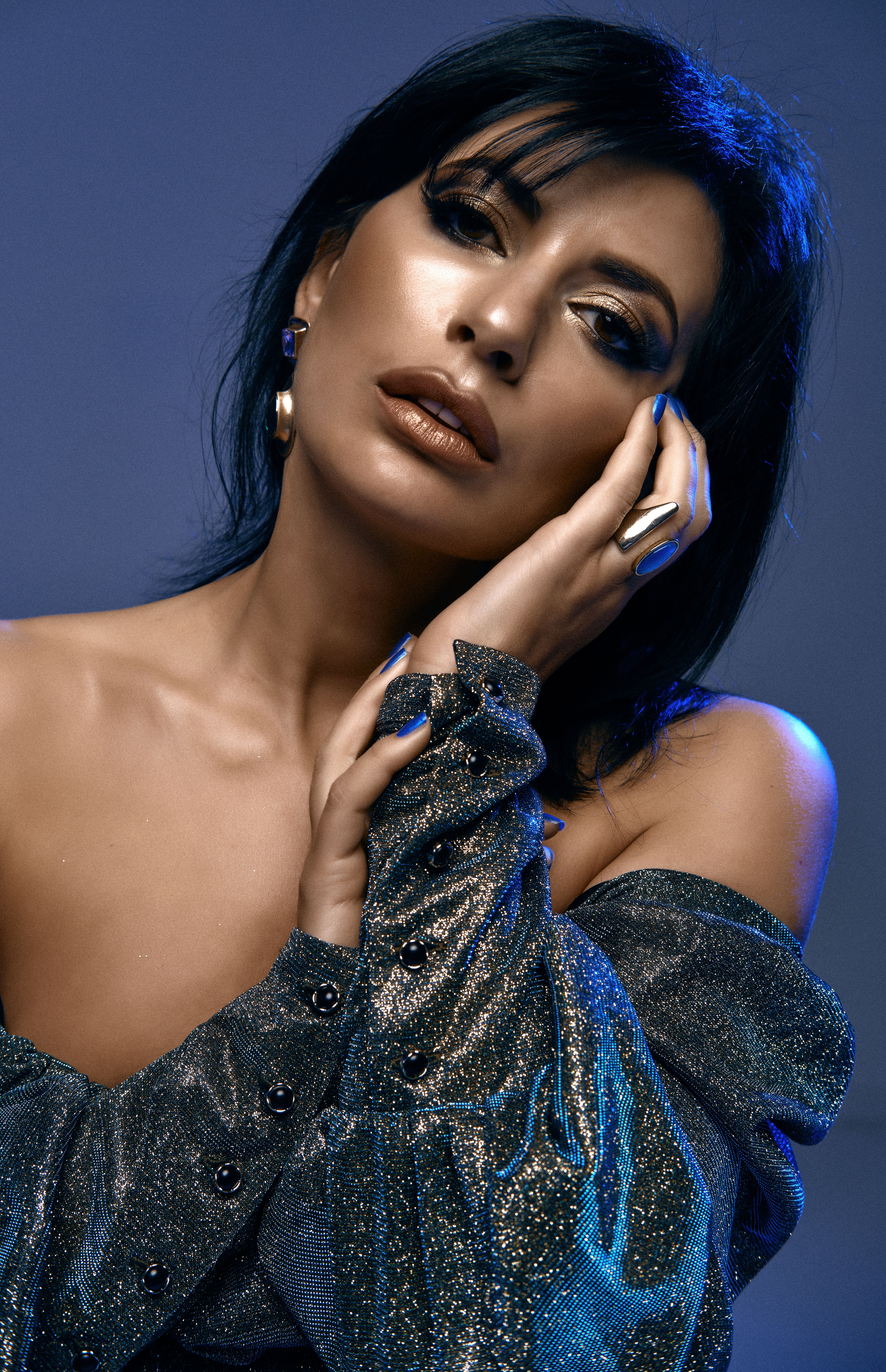 Elegant woman posing in a modern fashion portrait with metallic attire and blue lighting.