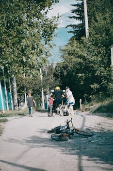 Children gather around bikes on a dirt road surrounded by trees in Almaty Province, Kazakhstan.