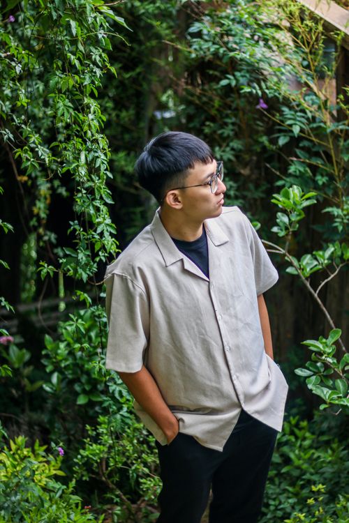 Free A man with black hair and eyeglasses poses outdoors surrounded by lush green plants. Stock Photo