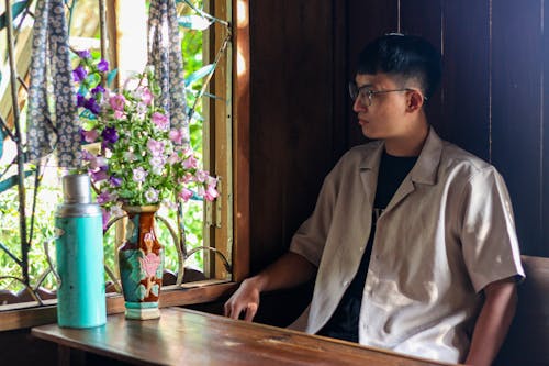 Man in Shirt Sitting by Table with Flowers