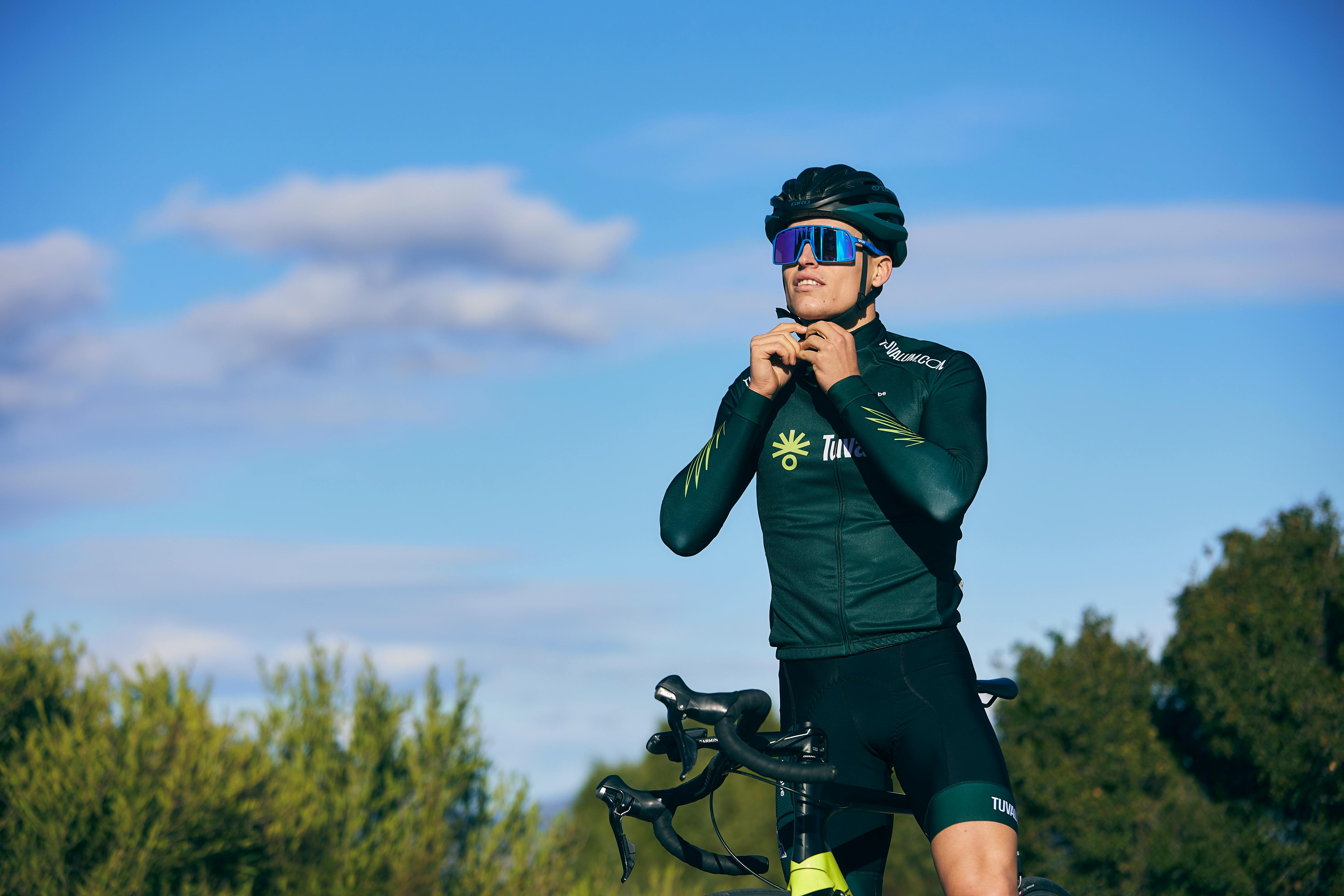 Cyclist adjusts helmet under clear sky, preparing for outdoor ride.