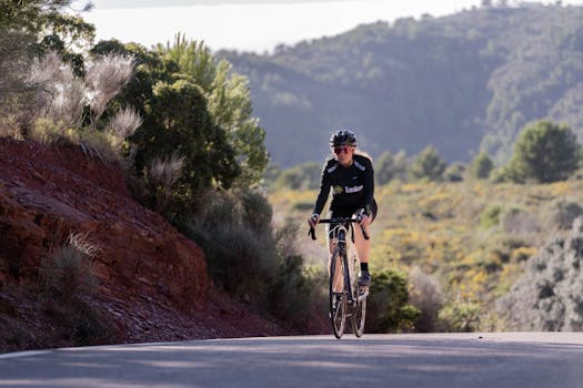 Woman cyclist riding a road bike uphill in a rural mountain landscape, showcasing endurance and sport.