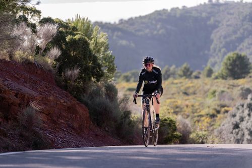 Free Woman cyclist riding a road bike uphill in a rural mountain landscape, showcasing endurance and sport. Stock Photo