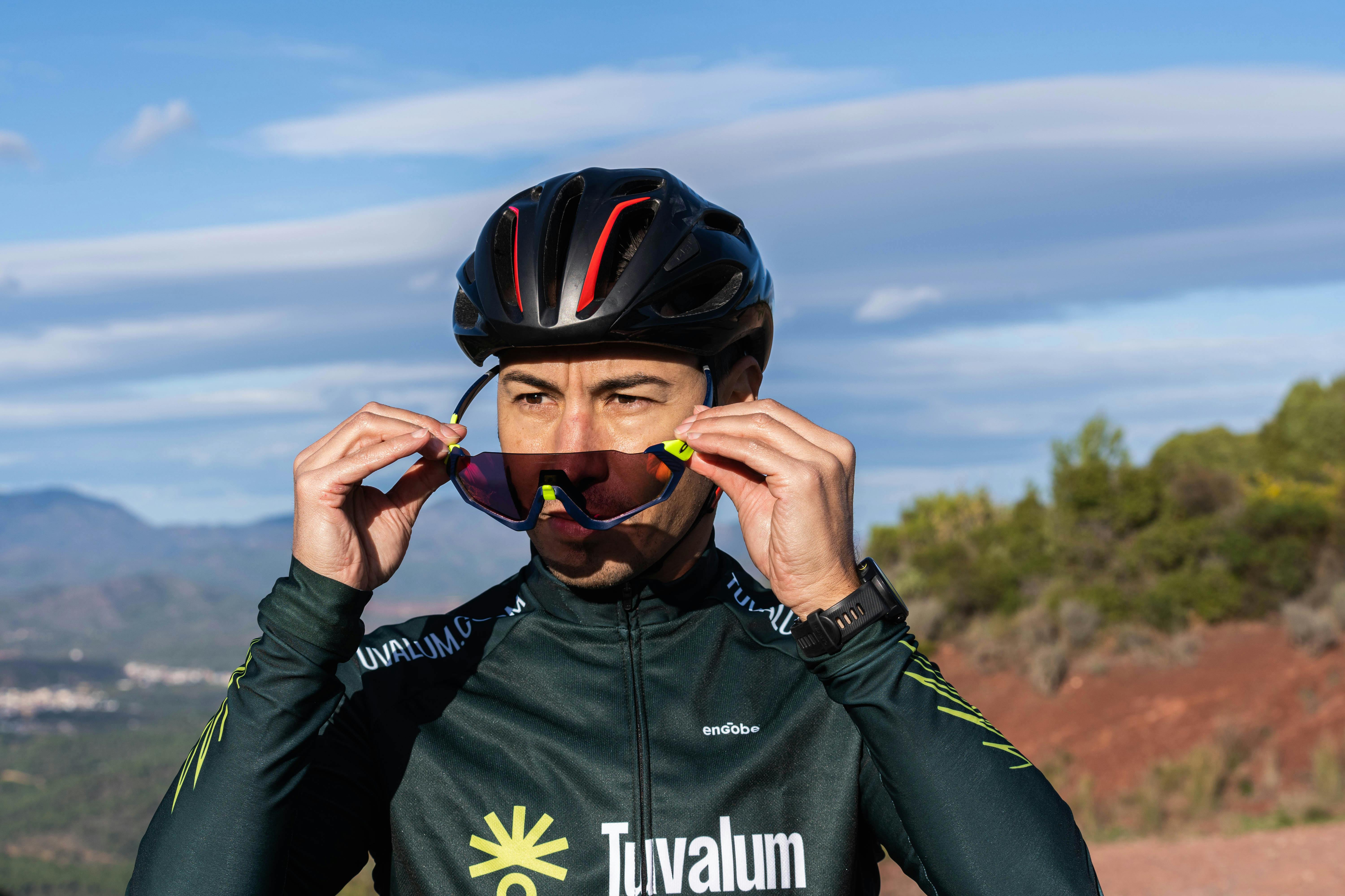 Adult male cyclist adjusting sunglasses outdoors, emphasizing sport and style.