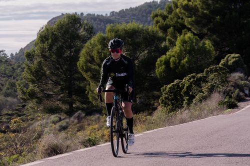 Free A woman cyclist wearing sportswear rides a road bike on a tree-lined rural path. Stock Photo