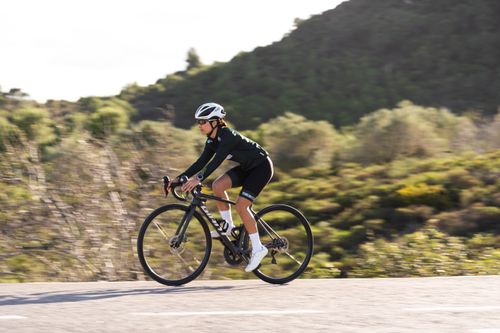 Free Sportswoman cycling on a scenic road surrounded by nature, showcasing athleticism and freedom. Stock Photo