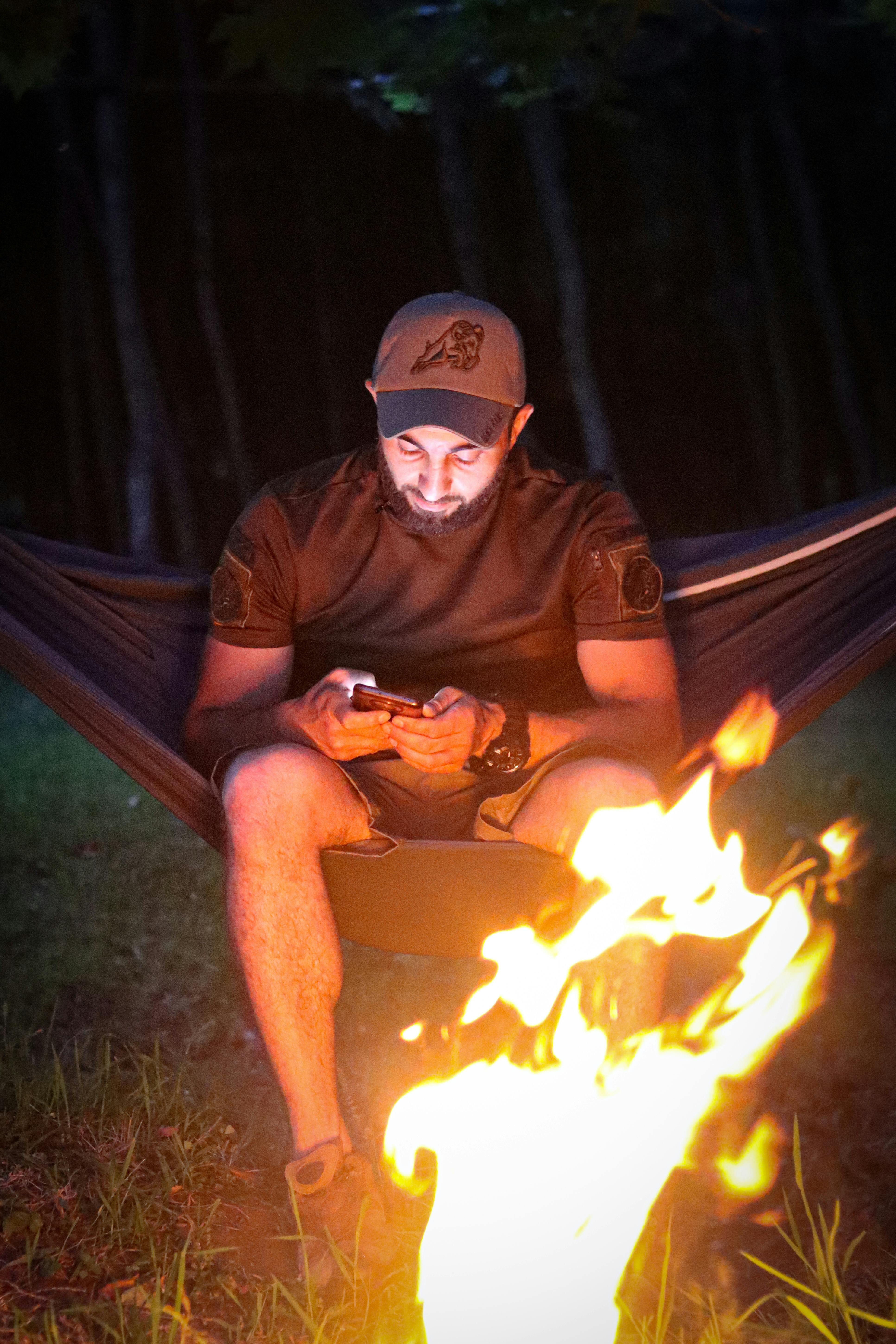 man sitting on hammock by bonfire