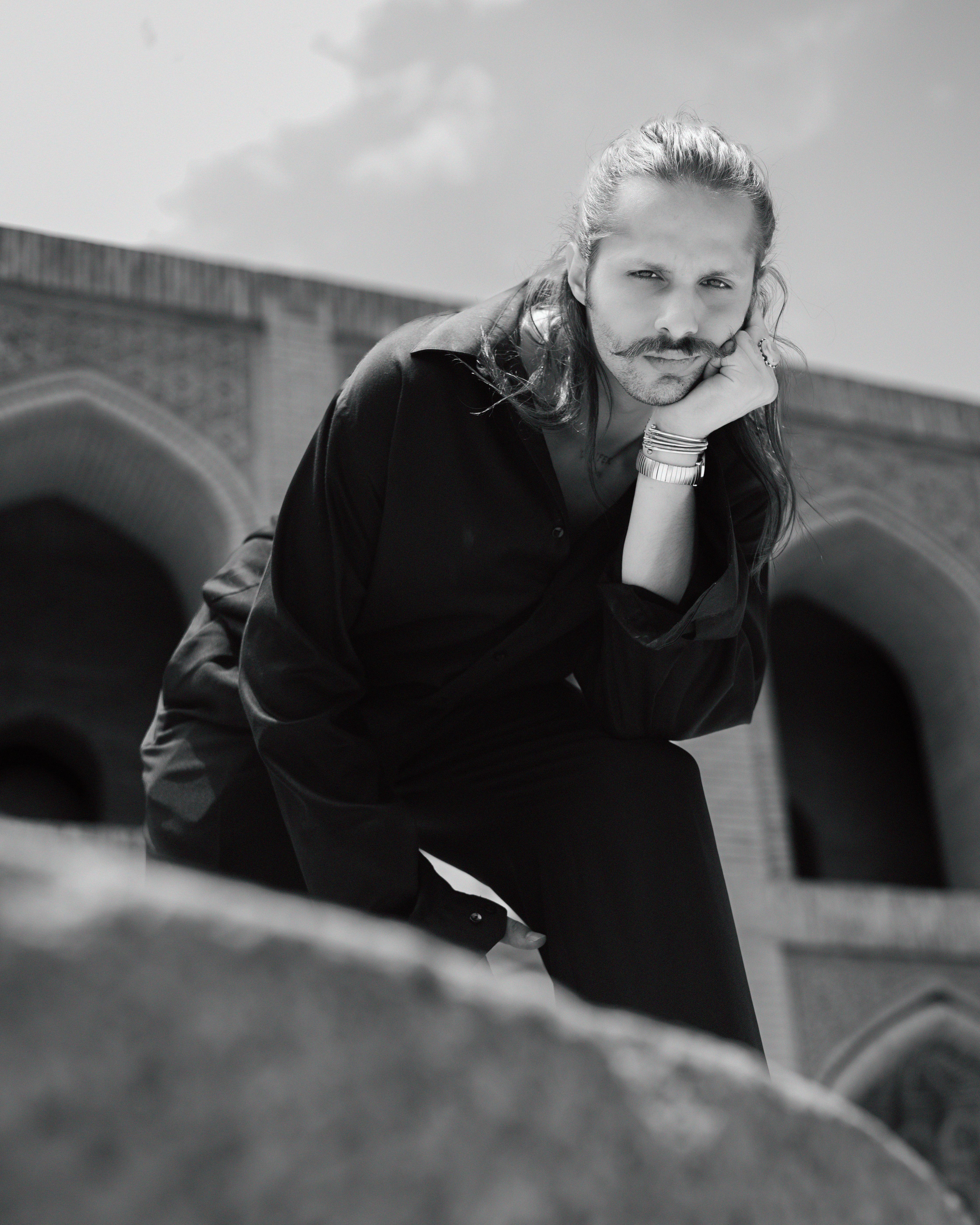 Black and white portrait of a fashionable man with mustache in front of historic architecture.