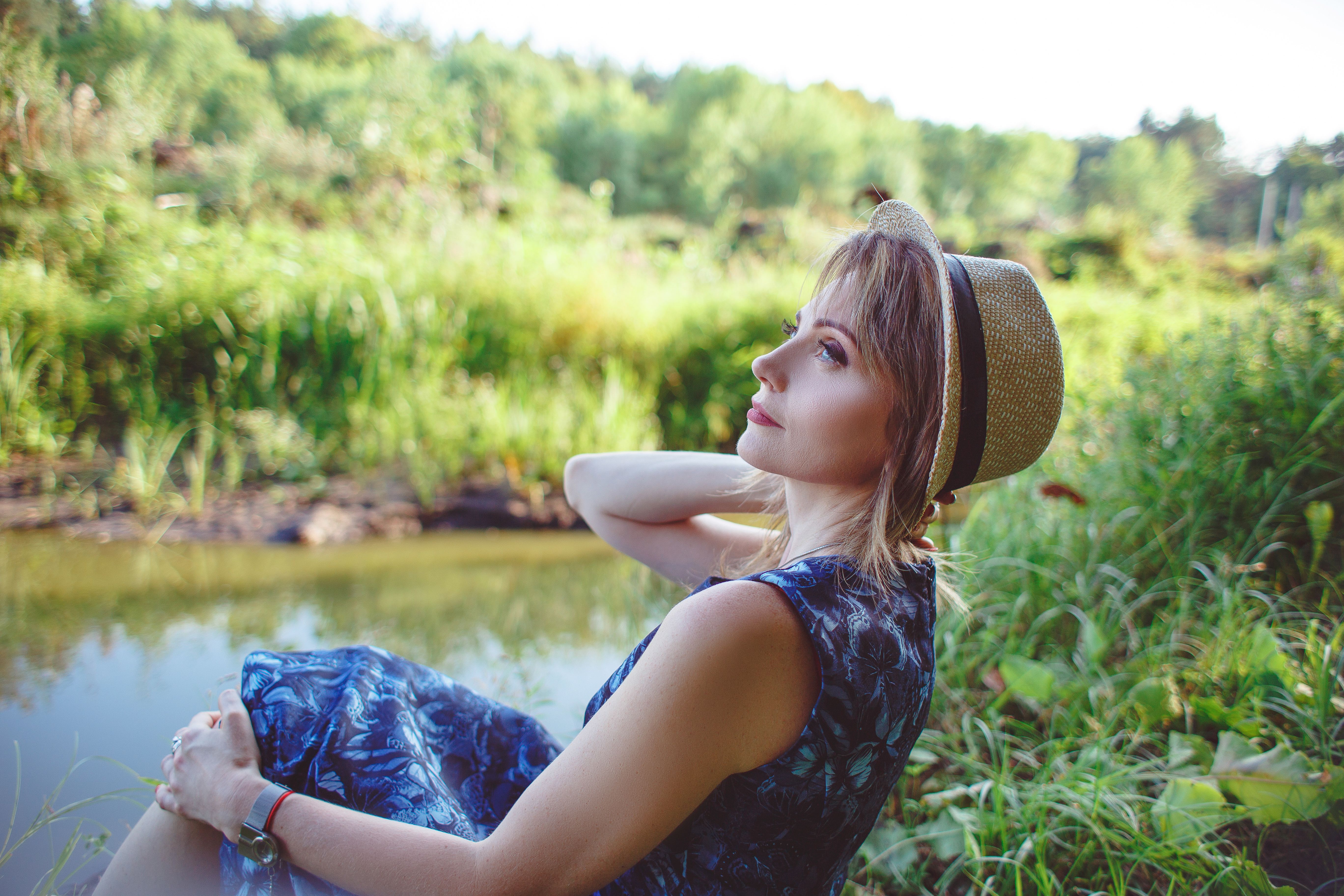 A woman in a summer hat relaxing by a river, enjoying the serene landscape.