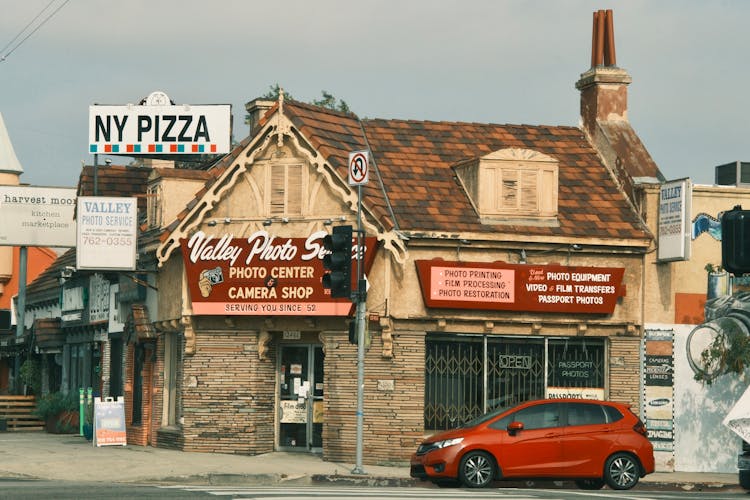 Red Car Parked By An Old Building With Small Shops, Valley Village, Los Angeles, USA