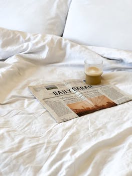 Newspaper and latte in a glass on a bed, perfect cozy morning setup.
