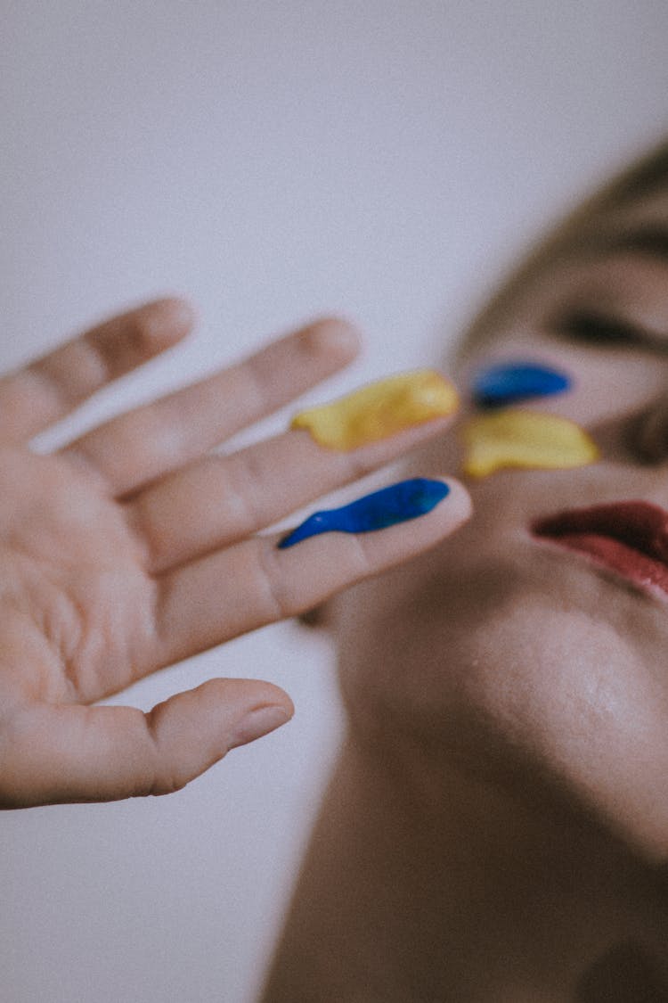 Woman With Blue And Yellow Paint On Her Hand And Face 