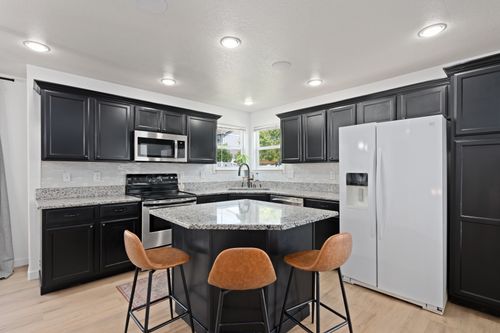 Free Spacious modern kitchen featuring black cabinets, granite countertops, and a white refrigerator. Stock Photo