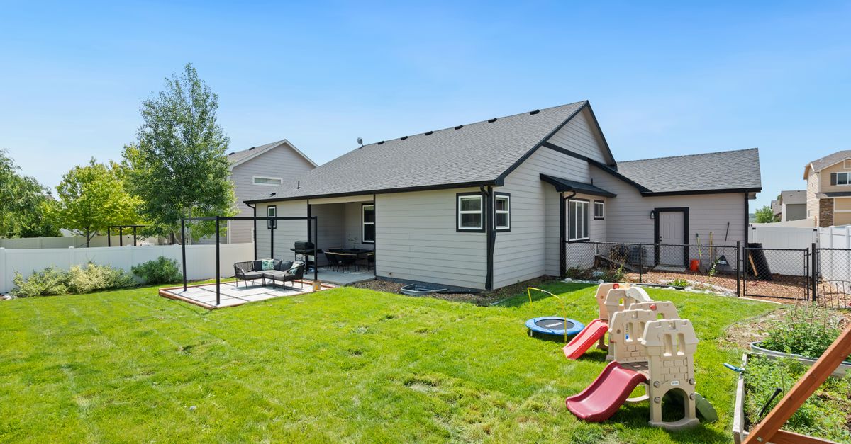 A peaceful suburban backyard featuring a children's play area and a cozy patio under a clear blue sky.