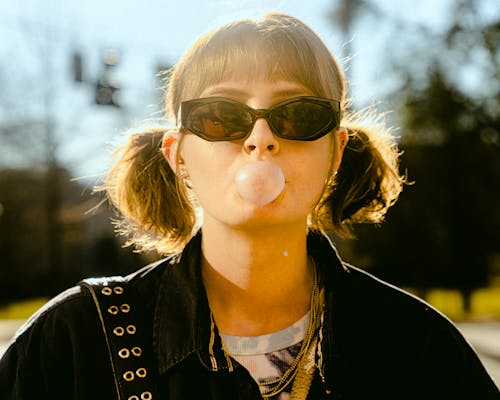 Young Woman in Sunglasses Blowing a Bubble Gum Balloon 
