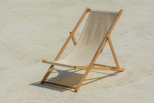 Free Minimalist outdoor scene featuring an empty sunlit deck chair on the beach, perfect for vacation themes. Stock Photo