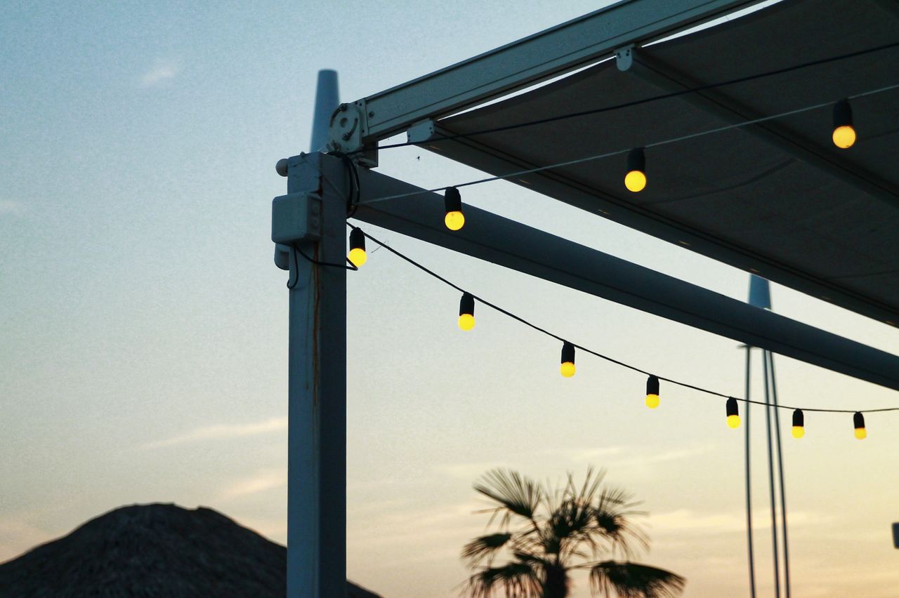 Warm string lights hanging from a metal patio frame at dusk