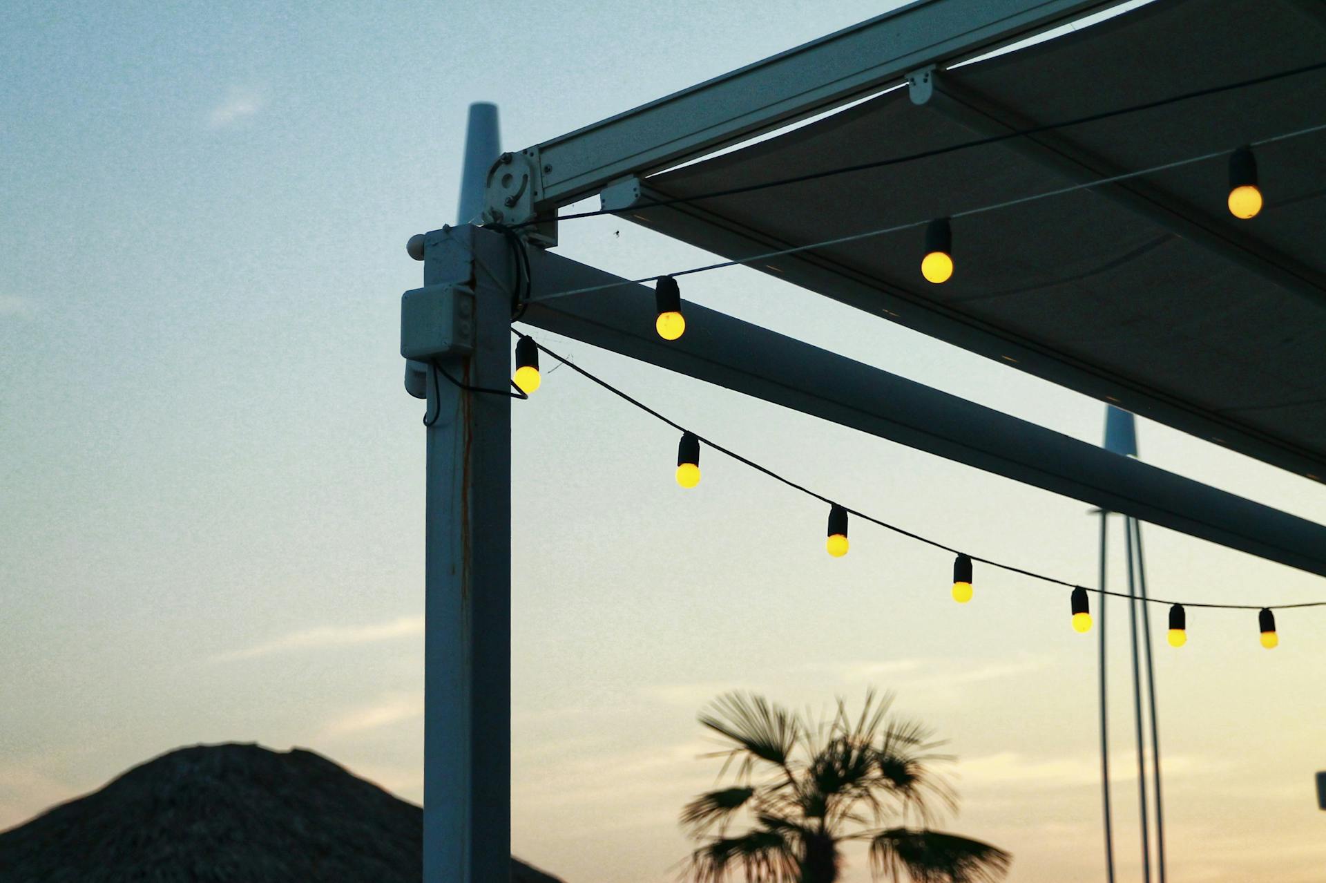 String lights hanging on a patio structure during sunset with palm trees in the background.