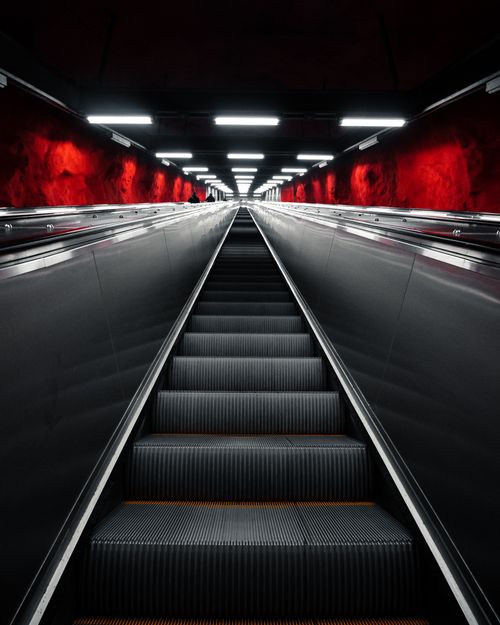 Free Low angle view of a modern escalator with striking red rock walls and overhead lights. Stock Photo