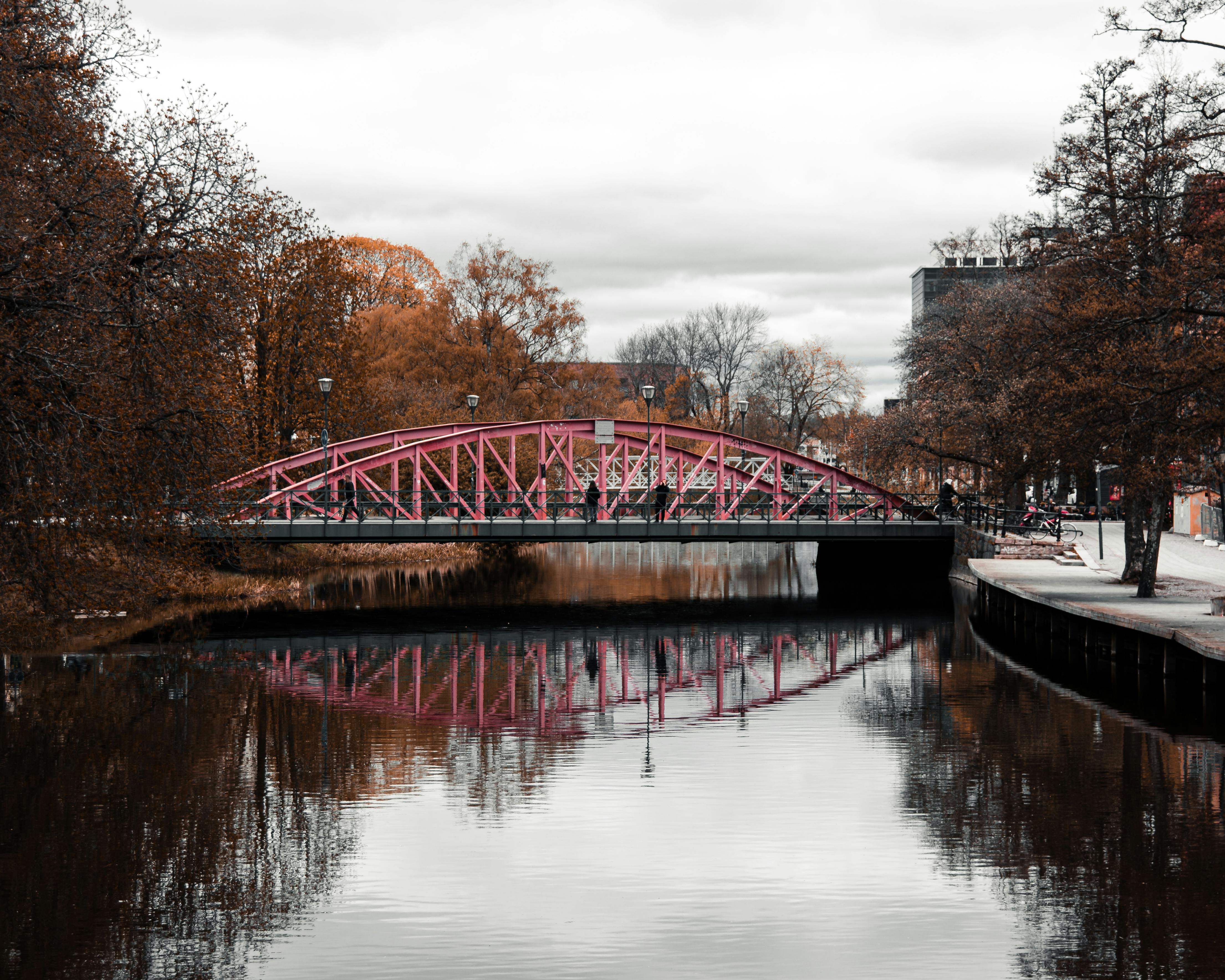 A striking pink bridge reflects on a calm river amidst Uppsala's autumn scenery, Sweden. - Uppsala