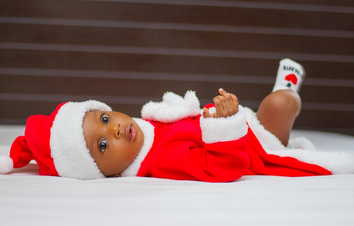 Baby Wearing Santa Claus Costume While Lying on Bed