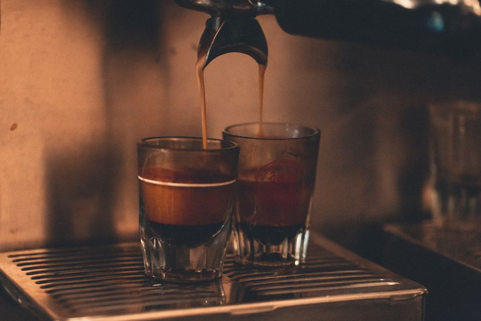 A single shot of espresso with reddish-brown crema being pulled into a small ceramic cup under a portafilter.