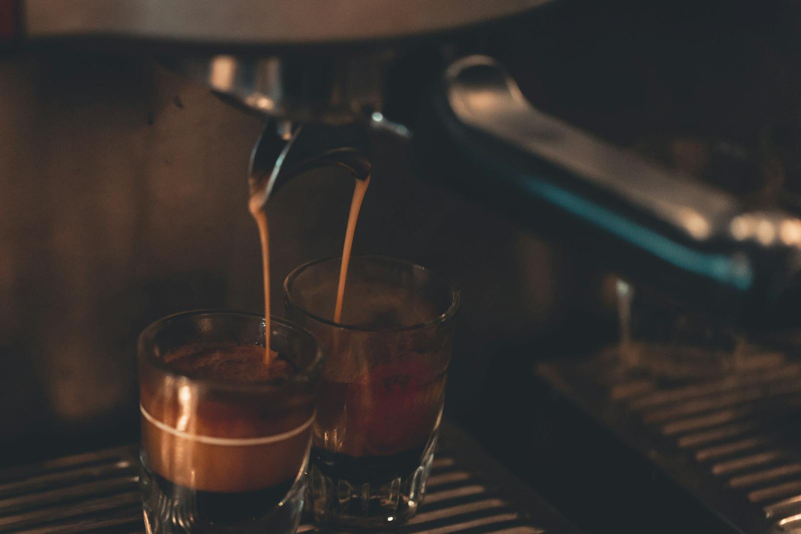Espresso pouring into two small glasses with crema forming