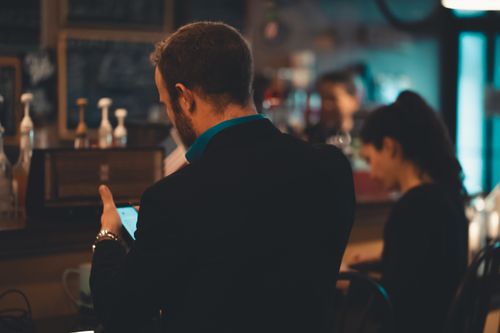 Free Adult man in a suit using a smartphone inside a cozy coffee shop setting. Stock Photo