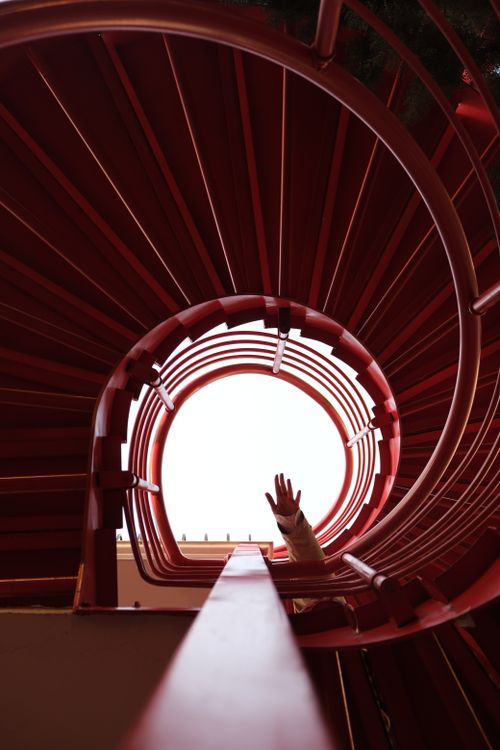 Free A captivating view of a red spiral staircase with a hand reaching upwards towards the open sky. Stock Photo