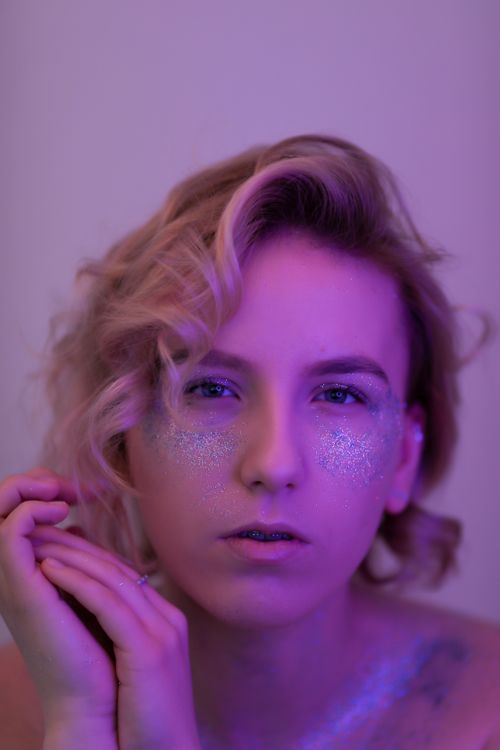 Free A vibrant portrait of a young woman with glitter makeup under pink lighting, exuding glamour. Stock Photo