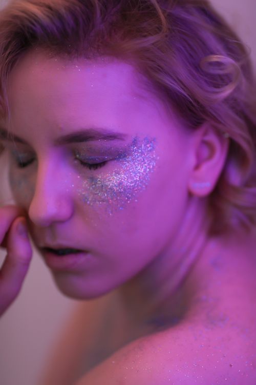 Free Close-up portrait of a woman with glitter makeup and eyes closed, bathed in purple light. Stock Photo