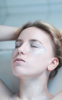 Dreamy portrait of a blonde woman with glitter makeup and eyes closed, creating an ethereal look.