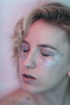 Close-up portrait of a woman with closed eyes and glitter makeup, captured artistically.
