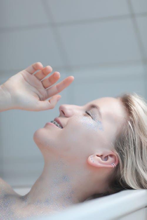 Smiling Young Woman with Glitter on Body Lying in Bathtub