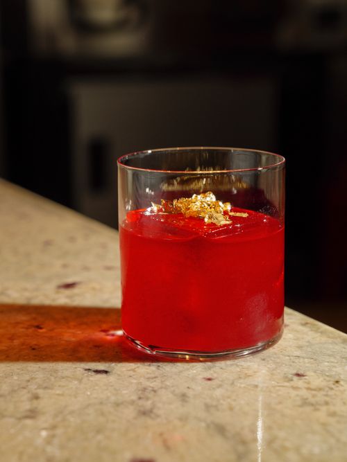 Free A vibrant red cocktail with gold leaf garnish on a marble countertop in warm lighting. Stock Photo