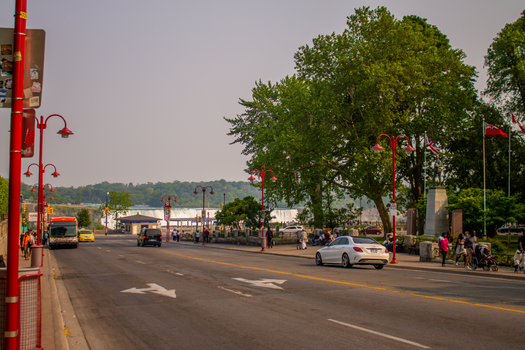 Busy urban street scene near the waterfront with red street lamps and vibrant greenery.