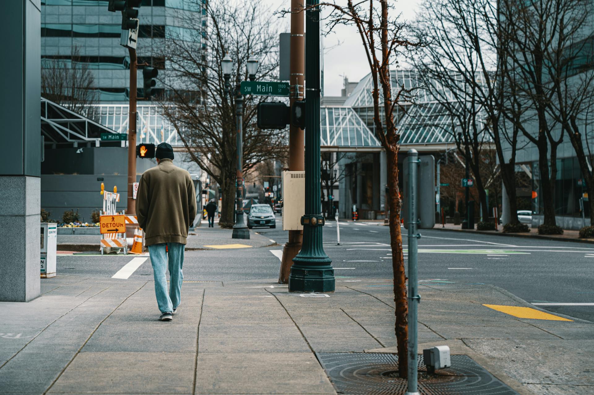 A man walks down Main Street in downtown Portland, Oregon, with urban buildings and winter trees.